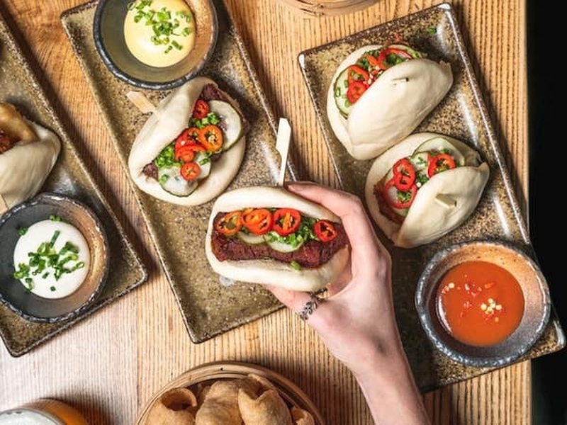A Person Holding A Bao And Other Asian Dishes From Cottonopolis Manchester