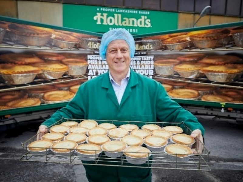 A Smiling Man In A Hairnet Holding A Tray Of Hollands Pies