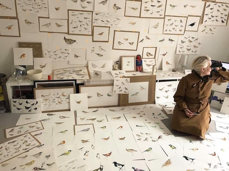 A Woman Looking Through Binoculars While Sitting On A Floor Covered With Paintings Of Birds For Fledge At Contemporary 6 Manchester