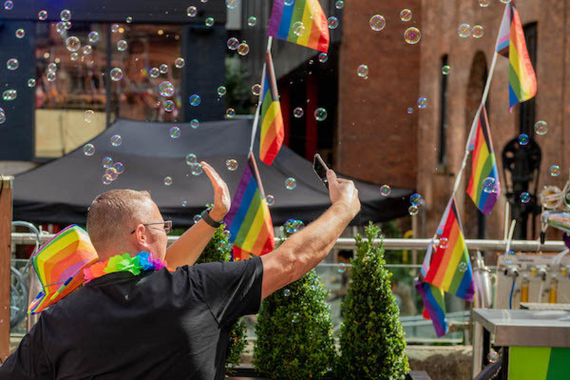 A Man In A Rainbow Lei With Rainbow Flags Takes Photos Of Bubbles At Manchester Pride 2021 Chris Keller Jackson