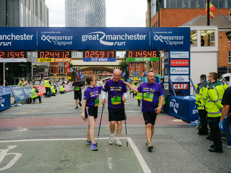 Three people helping each other over the finishing line in the Great Manchester Run