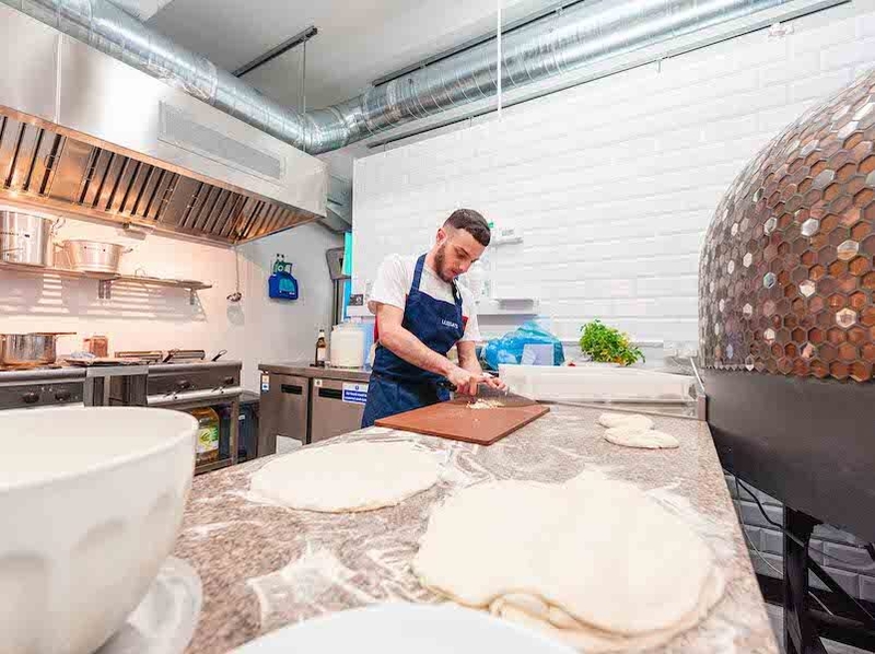 A Chef Chops Garlic Surrounded By Pizza Dough At Luisas Radcliffe