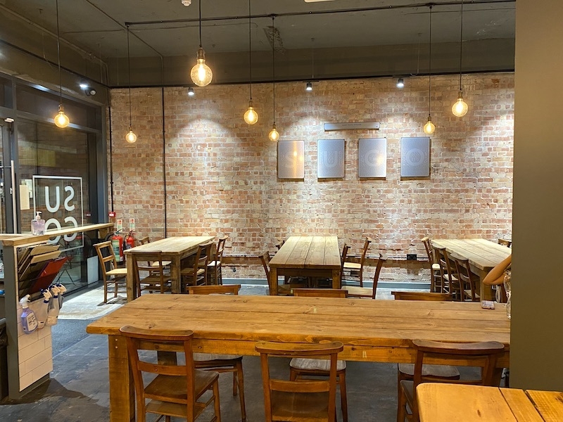 The Interior Of Sugo In Sale Manchester With Bare Brick Walls And Wooden Tables